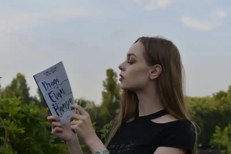 Alina Munteanu, cunoscută ca The Rockstar Reader, povestește despre experiența sa la Pop-Up Book Club. În imagine, Alina este surprinsă citind cartea ‘Dragă Evan Hansen’, într-un cadru natural, cu expresie concentrată și relaxată. Participarea la Pop-Up Book Club, alături de cititori pasionați, i-a oferit momente de introspecție, bucurie și conexiune, transformând fiecare întâlnire într-o experiență memorabilă pentru iubitorii de cărți.